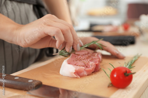 Female chef preparing meat on wooden board at table, closeup