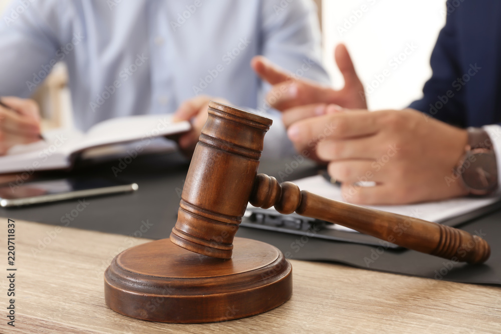 Gavel and blurred lawyer working with client on background Gavel and blurred lawyer working with client on background