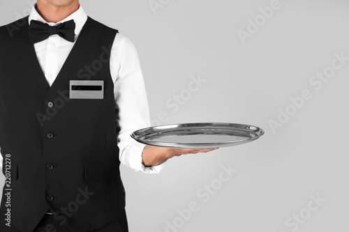 Waiter holding metal tray on grey background