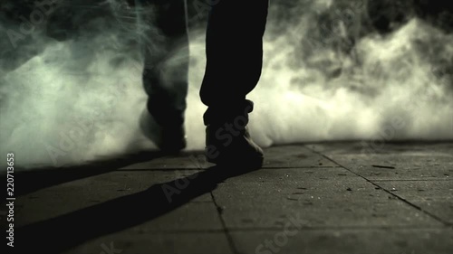 The legs of a man walking near the cloud of a smoke. slow motion photo