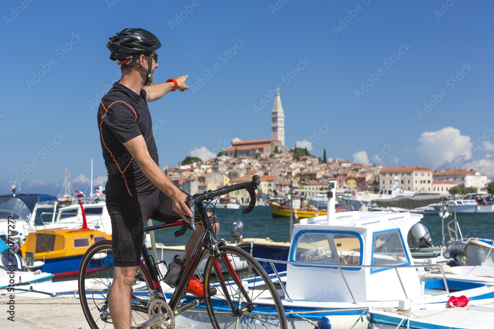 Naklejka premium Kroatien, Istrien, Rovinj, Portrait Rennradfahrer bei Pause am Hafen zeigt Richtung Sv Eufemija Kirche