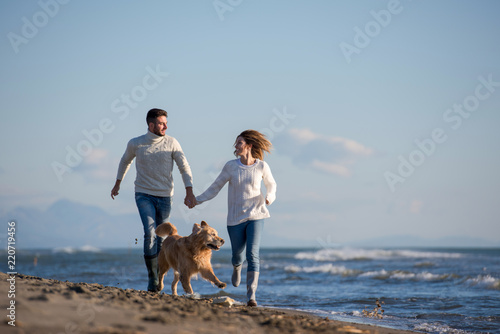 couple with dog having fun on beach on autmun day photo