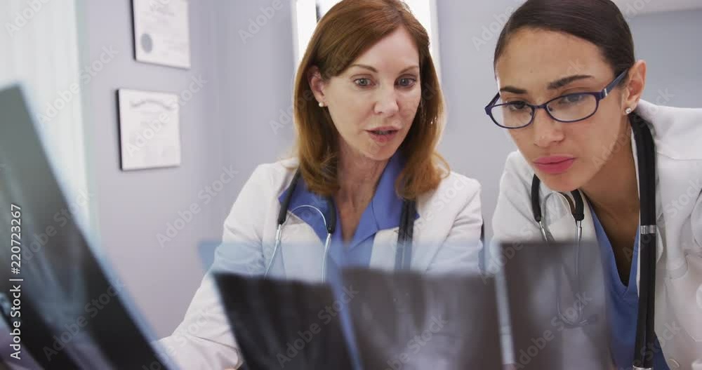 Young medical colleague discussing x rays of patient with senior doctor Young medical colleague discussing x rays of patient with senior doctor
