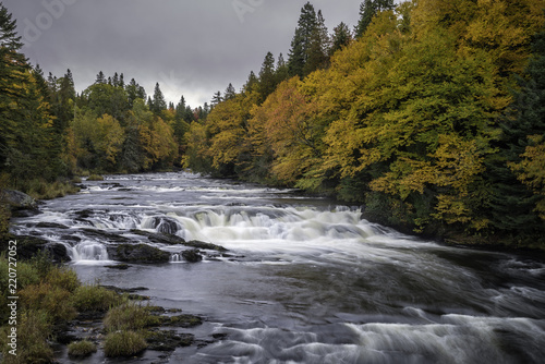 Waterfalls and rapids on a river surrounded by Fall foliage on an overcast day in New Hampshire
