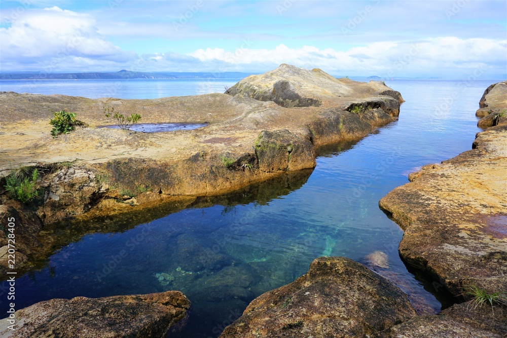 Fototapeta premium calm inlet of water between pale brown rocks, blue sky with white clouds
