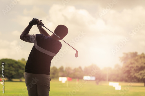 Man hitting golf shot with club on course at evening time.
