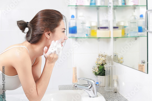 Woman happy cleanses the skin with foam in bathroom.