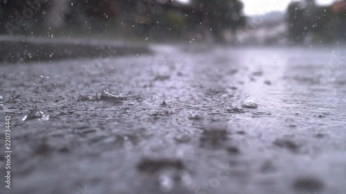SLOW MOTION CLOSE UP: Autumn rain water drops falling into big puddle on asphalt, flooding the street. Road floods due to the heavy rain in wet season. Raindrops falling down onto submerged road
