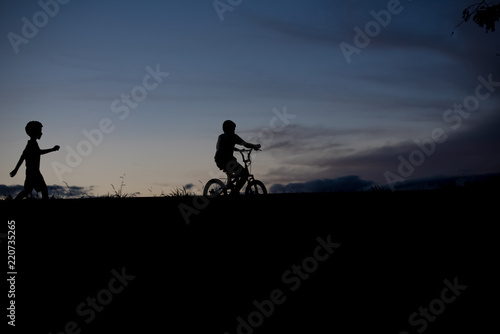 Silhouette of a boy riding a bicycle and another boy walking - outdoors