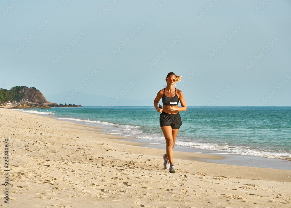 Slender woman is running on the beach with a smart phone on a sunny morning
Slender woman is running on the beach with a smart phone on a sunny morning