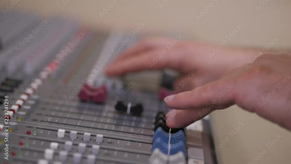 Hands of Audio engineer working on a professional analog console, moving faders, mixing music