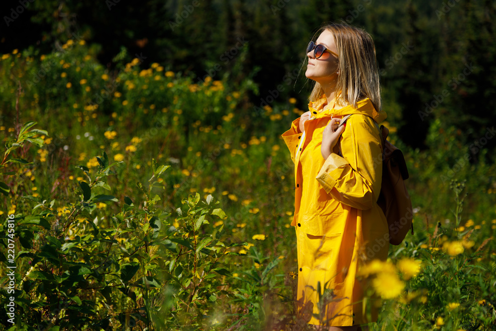 stylish hipster woman in yellow raincoat traveler with backpack on top of mountains, travel concept, travel standing in the mountain.