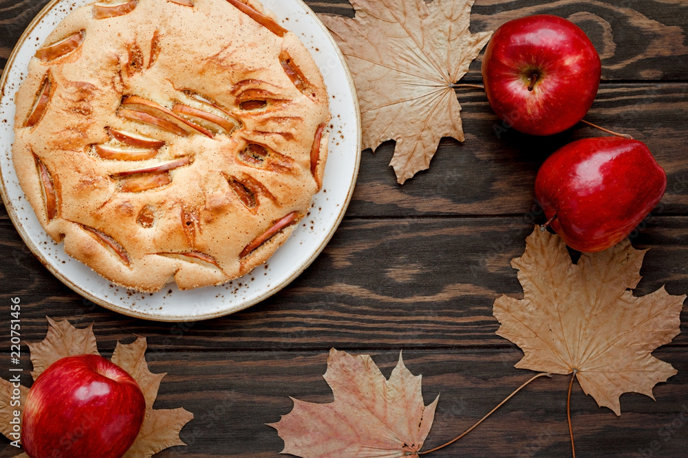 Tasty homemade season apple pie surrounded by maple dead leaves and red apples. Autumn bakery, cosy holidays. Copy space.