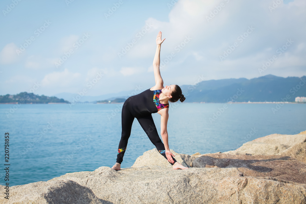 Beautiful young woman in sports jumpsuit doing yoga exercise outdoors with sea views