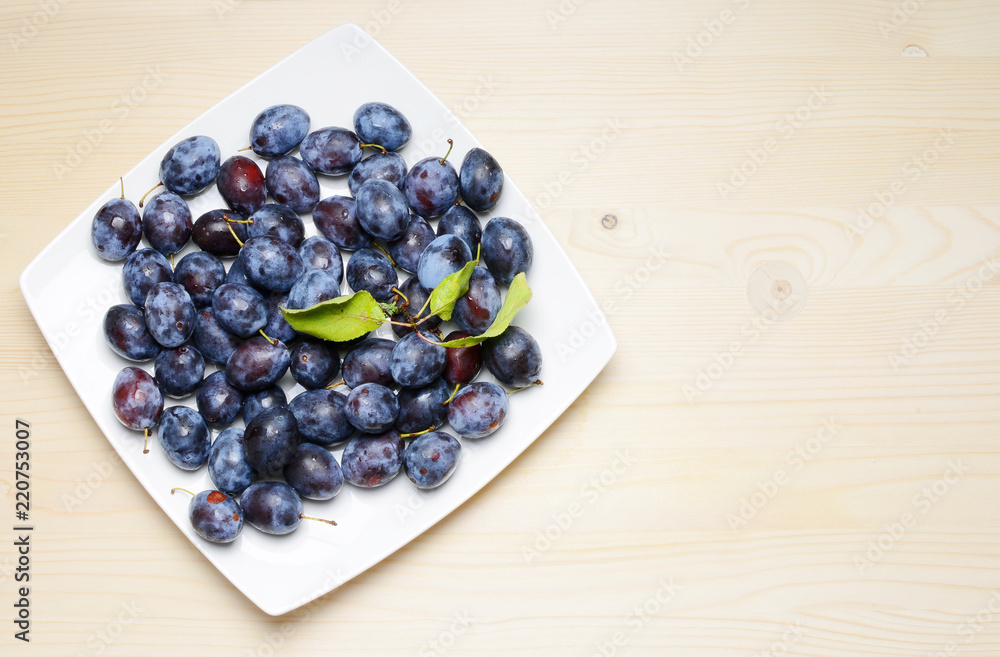 Fresh plums with leaves on a wooden table background. Flat lay composition. Fresh plums with leaves on a wooden table background. Flat lay composition.
