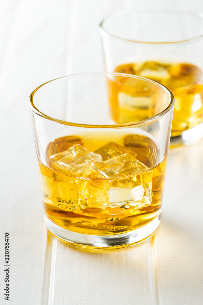 Glass of alcoholic drink with ice cubes on white table. Glass of alcoholic drink with ice cubes on white table.