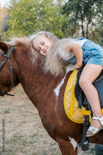 A cute little blonde girl is sitting on a pony in autumn.