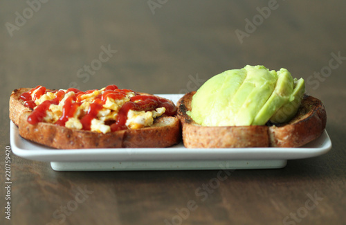 Healthy breakfast. Toasted whole wheat bread, omelet(Omelette) with tomato sauce (ketchup) and fresh avocado on white dish on dark wood background