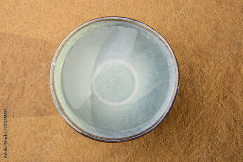 Fresh water in bowl on sand background. Blue ceramic bowl with clean drink water outdoors, top view. 
