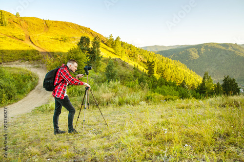 Young guy photographer takes pictures of nature with mountains on a SLR camera. photo