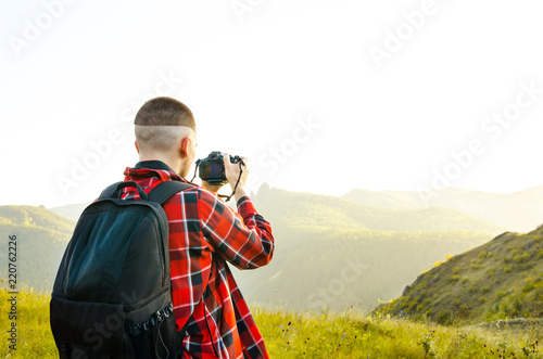 Young guy photographer takes pictures of nature with mountains on a SLR camera. photo