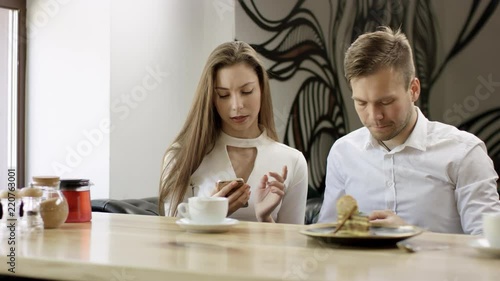 Two young people is sitting in a cafe. Man and woman are smiling and sitting in the cafe at the table during break. Couple is talking and drinking coffee. They aretyping mesagies on their moile phones photo