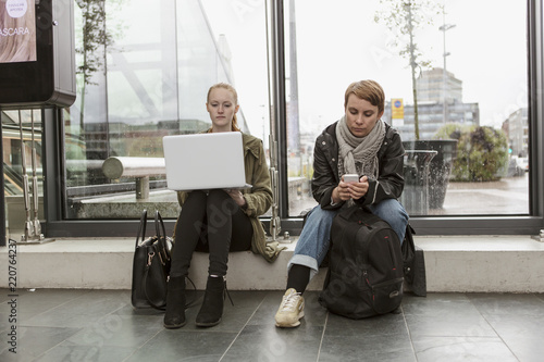 Full length of friends using technologies while waiting at station photo