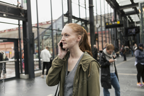 Young woman talking on mobile phone with friend in background at city photo