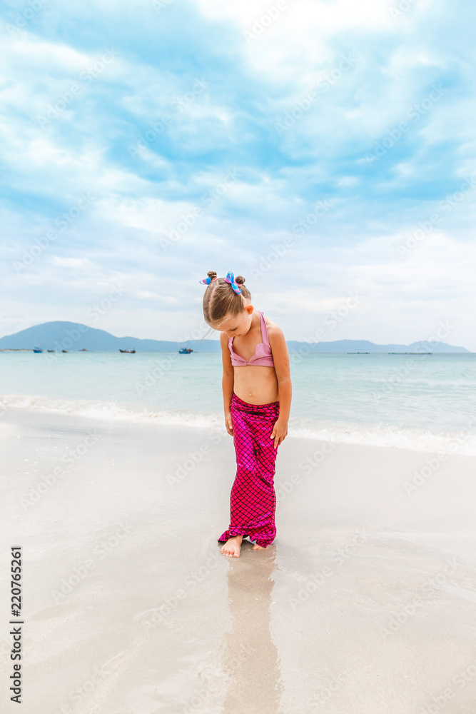 Little beautiful girl dressed in swimsuit as a mermaid stands on the seashore