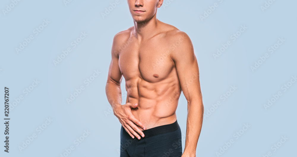Horizontal cropped image of fitness male model in black underwear showing his abdominal torso on a blue background. Portrait of sporty healthy strong athletic man with sexy abdomen posing in studio.