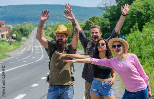 Travellers try to stop car. Begin great adventure in your life with hitchhiking. Friends hitchhikers travelling summer sunny day. Company friends travelers hitchhiking at edge road nature background