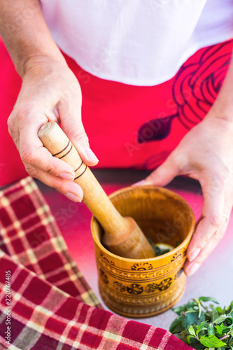A woman holds a rustic wooden mortar in her hands and kneads peppermint for cooking or cospectology. Slow life Homemade concept