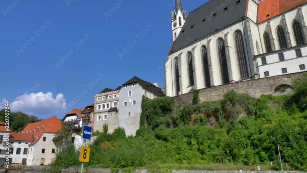 View of Saint Vitus church in Cesky Krumlov, Czech Republic surrounded by lush green nature and the town's buildings by the Vltava river View of Saint Vitus church in Cesky Krumlov, Czech Republic surrounded by lush green nature and the town's buildings by the Vltava river