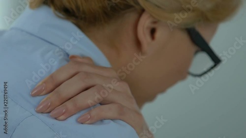 Female employee concerned about shoulder pain at workplace, self-massage therapy photo