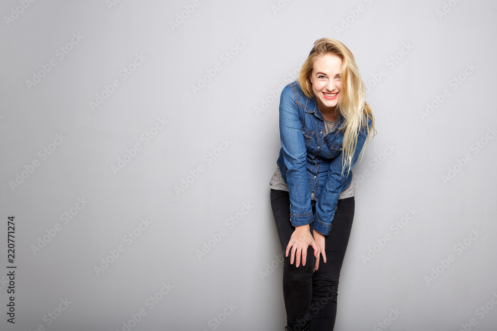 happy young blond woman leaning on knee against gray background happy young blond woman leaning on knee against gray background