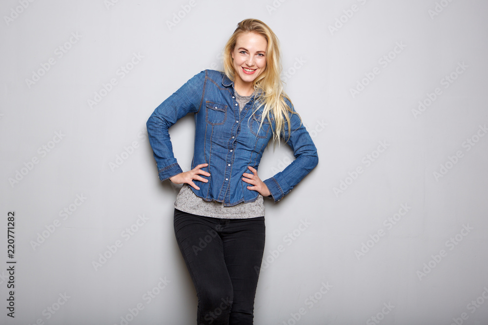 young blond woman smiling with hands on hip against gray background young blond woman smiling with hands on hip against gray background