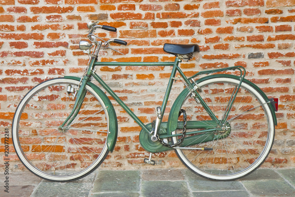 Old green bicycle parked against a brick wall