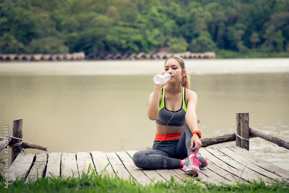 Young beautiful woman in sports dress drinking water after workout near the river outdoors.
