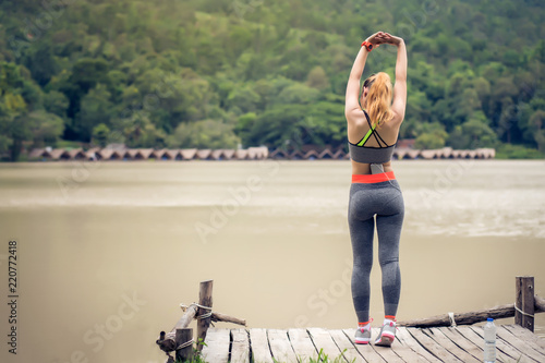 Young beautiful woman in sports dress stretching before exercise near the river outdoors. © amnaj