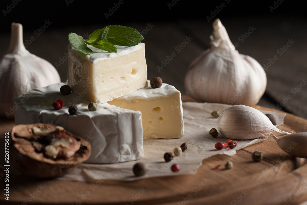 Camembert and brie cheese on wooden background with tomatoes, letuce and garlic. Italian food. Dairy products.