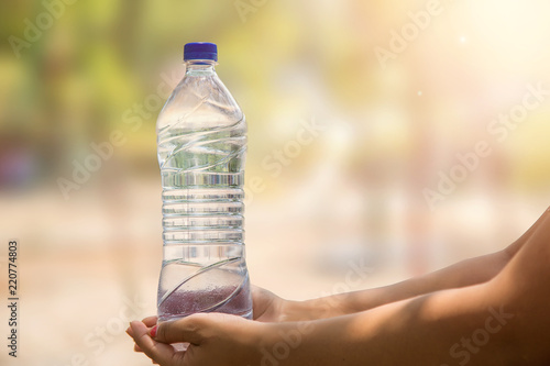 Photography Water bottle in woman's hand on blurred green bokeh background