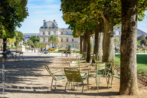 The Luxembourg garden in Paris, France, by a sunny summer morning with people biking, strolling or resting on metal lawn chairs and the Luxembourg palace, seat of the Senate in the background. © olrat