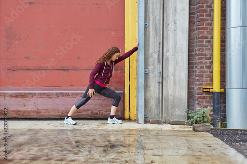 Frau macht Dehnübung gegen eine Mauer