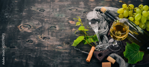 A bottle of white wine with glasses and grapes. Leaves of grapes. Top view. On a black wooden background. Free space for text.