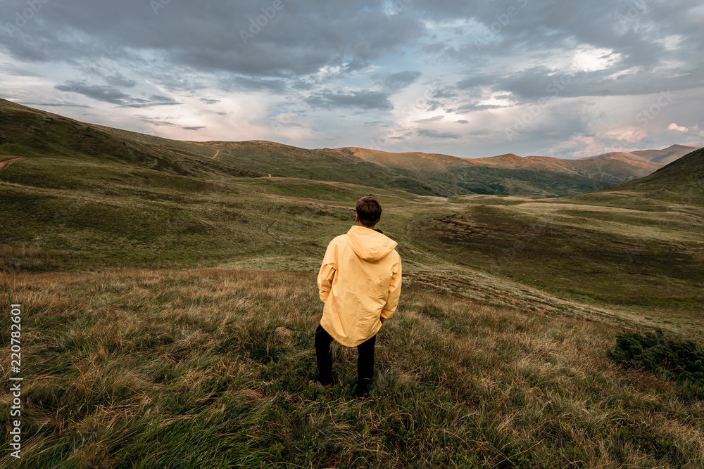A young guy in a yellow raincoat on top of a mountain. Carpathians, Ukraine
