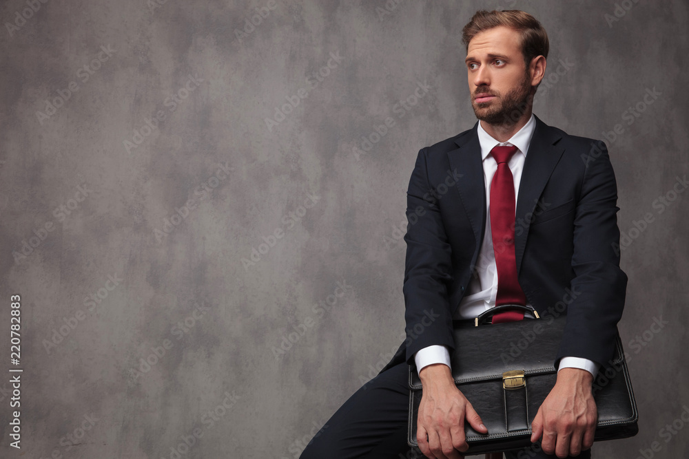 seated young businessman holds suitcase and looks to side seated young businessman holds suitcase and looks to side