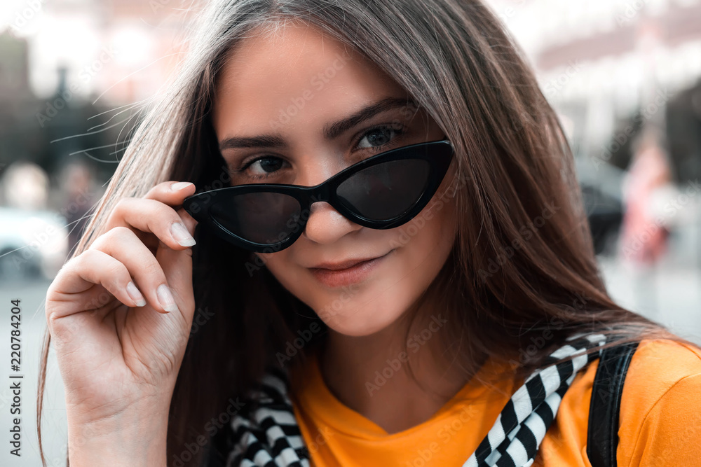 Close up fashion portrait of young woman with sunglasses against street  background. Caucasian female fashion model posing with glasses.