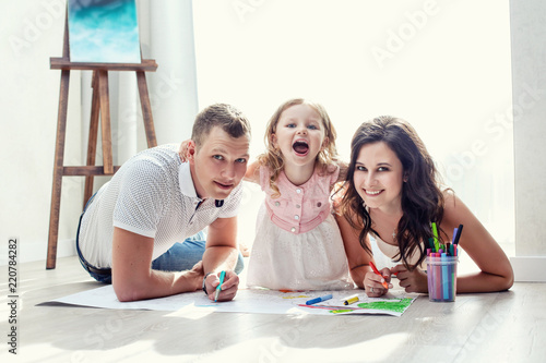 Family mother  father and daughter happy and beautiful with smiles at home together draw lying on the floor