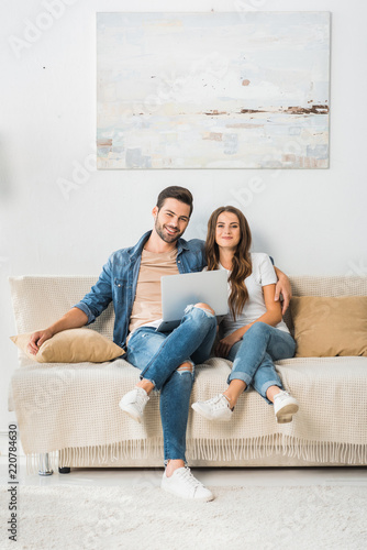 smiling young couple sitting on sofa with laptop at home