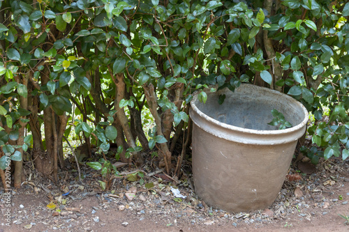 A large empty grey metal rusted pot next to a green hedge in a garden